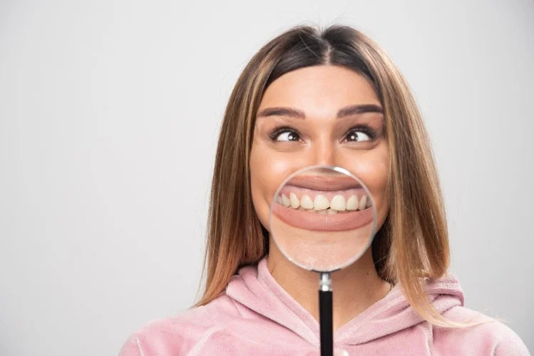 Seorang gadis memegang kaca pembesar, menunjukkan gigi hadapannya dari dekat